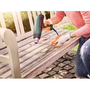 Bosch Heißluftgebläse UniversalHeat 600 entlackt Holzbank. Grünes Gerät, orangefarbener Griff, im Einsatz im Garten.