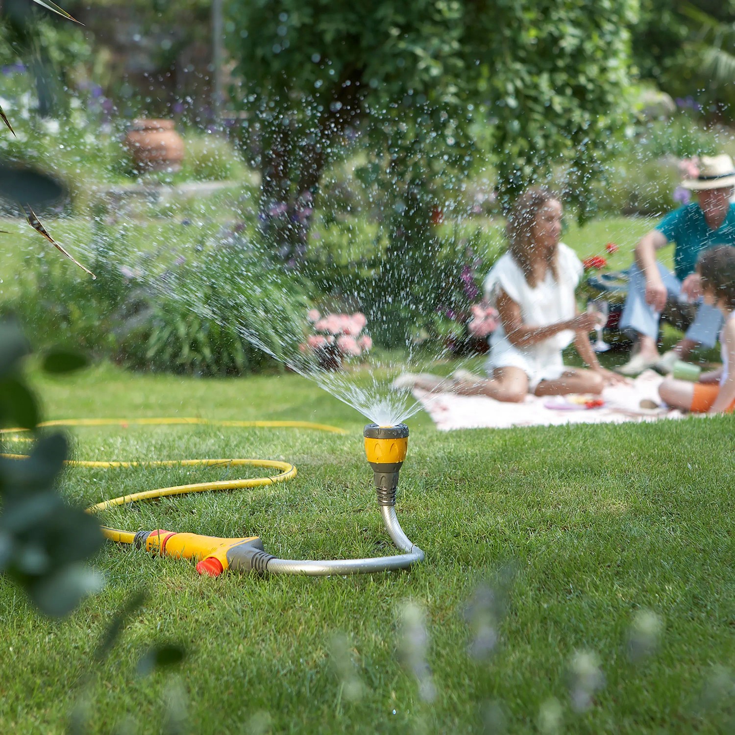 Hozelock Flexi Spray 4in1 Gartenbrause als Rasensprenger im Garten mit Familie im Hintergrund.