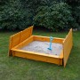 Holz Sandkasten Tessa 140x140 cm mit klappbarer Abdeckung und Sandspielzeug im Garten.
