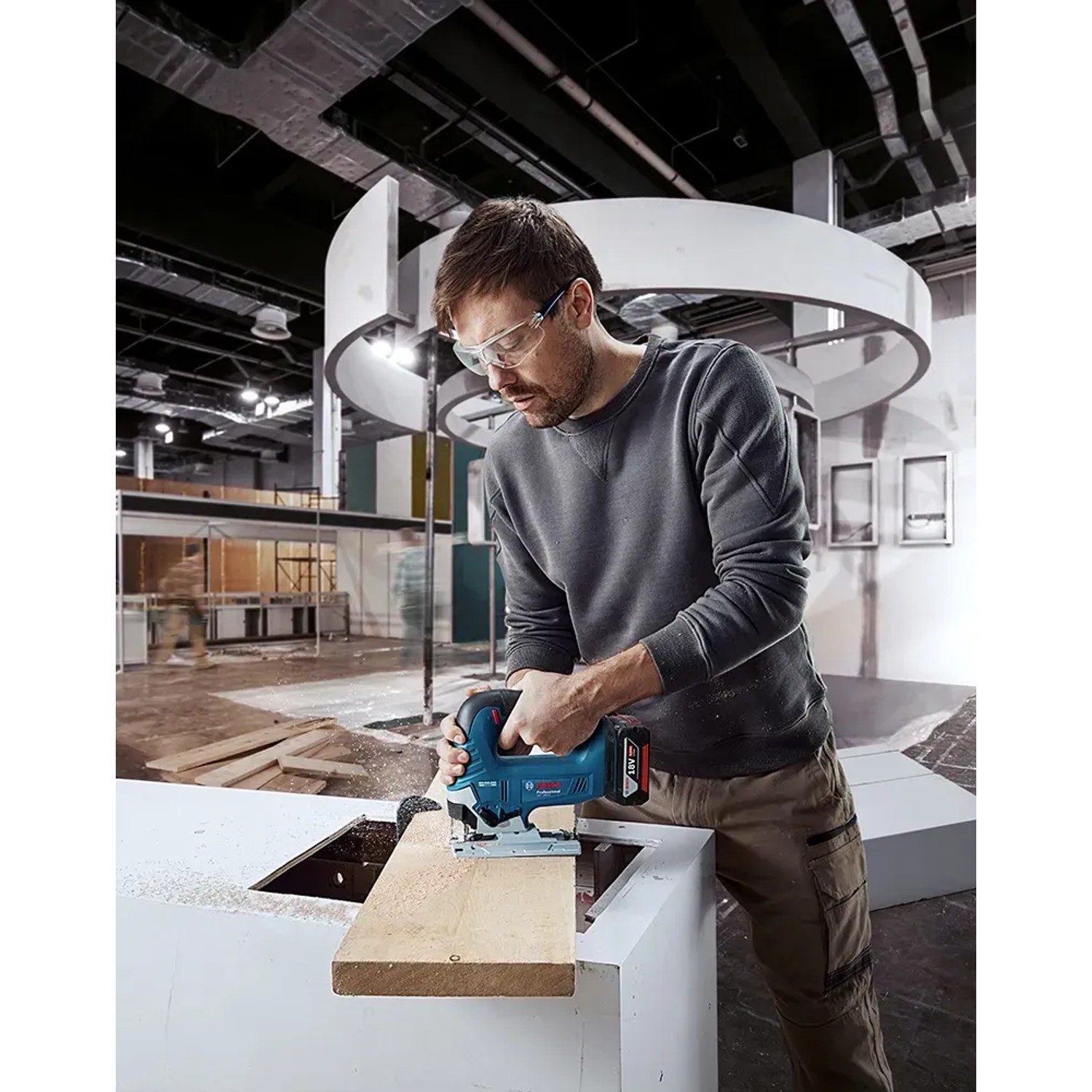 Mann sägt Holz mit Bosch Professional Akku-Stichsäge GST 18 V-125 B. Stichsäge in Blau.