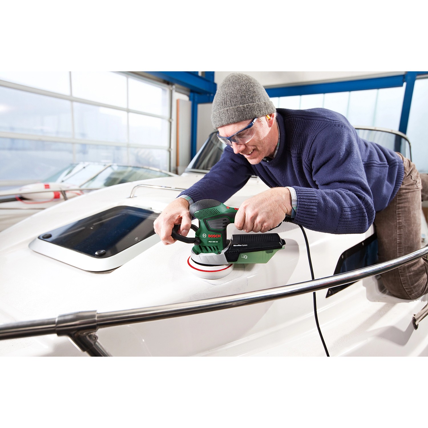 Mann schleift Boot mit Bosch Exzenterschleifer PEX 400 AE. Schleifmaschine mit Staubabsaugung.