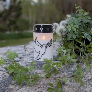 Weißes LED-Grablicht mit Taubenmotiv, flackerndem warmweißem Licht und Timerfunktion, 12cm hoch, auf Stein im Garten.