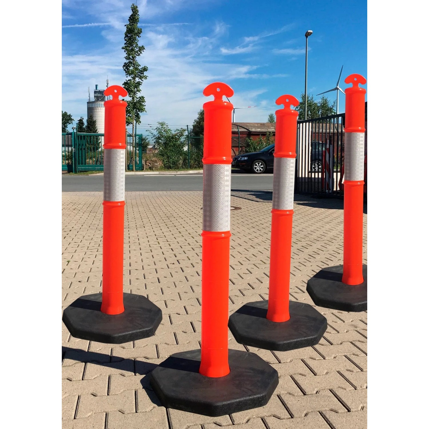 Orangefarbene UvV FLEX Absperrpfosten mit Reflexstreifen und schwarzer Fußplatte.