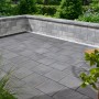 Verlegte Kann Pflastersteine Quadera, 30x30 cm, Vulkananthrazit, auf einer Terrasse mit Mauer.