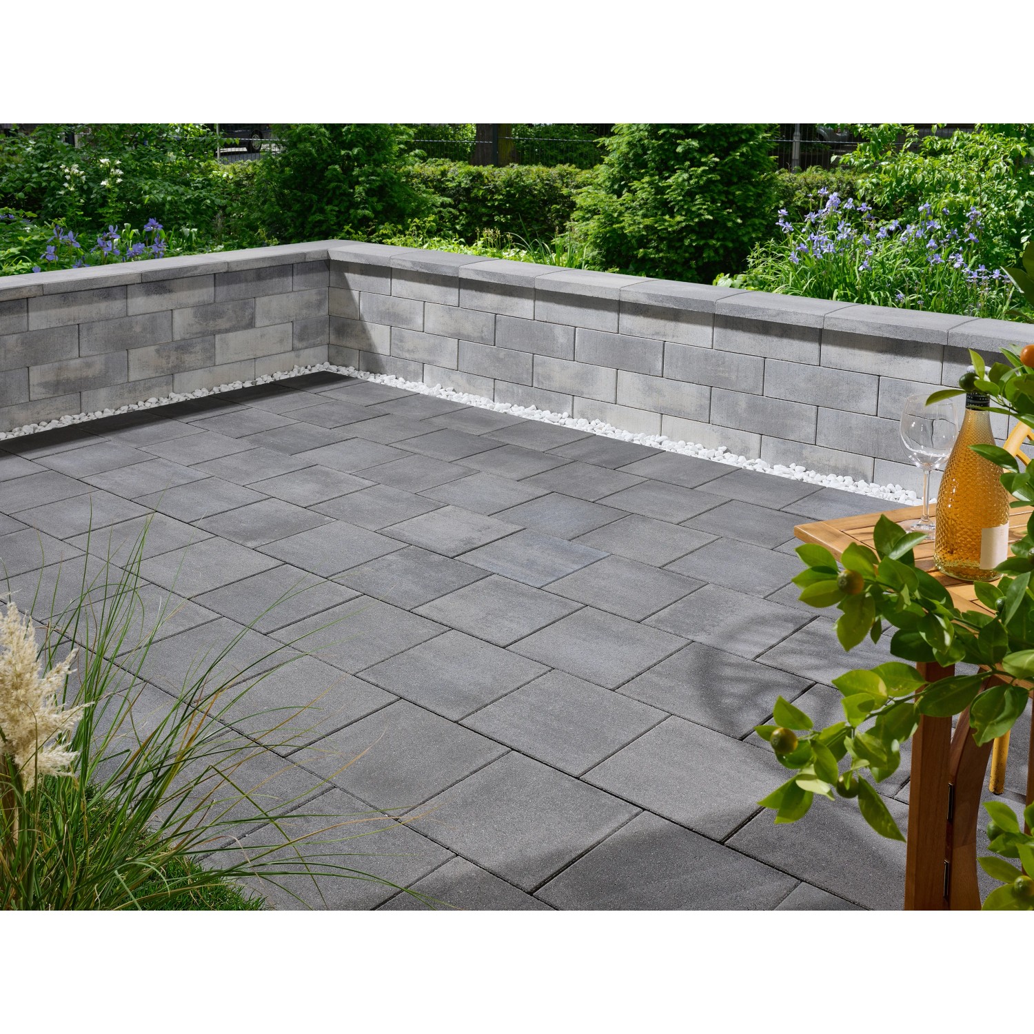 Verlegte Kann Pflastersteine Quadera, 30x30 cm, Vulkananthrazit, auf einer Terrasse mit Mauer.