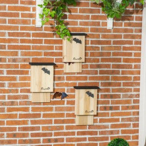 Drei PawHut Fledermauskästen aus Naturholz mit Fledermausmotiv an Ziegelwand. Eine Fledermaus fliegt davor.
