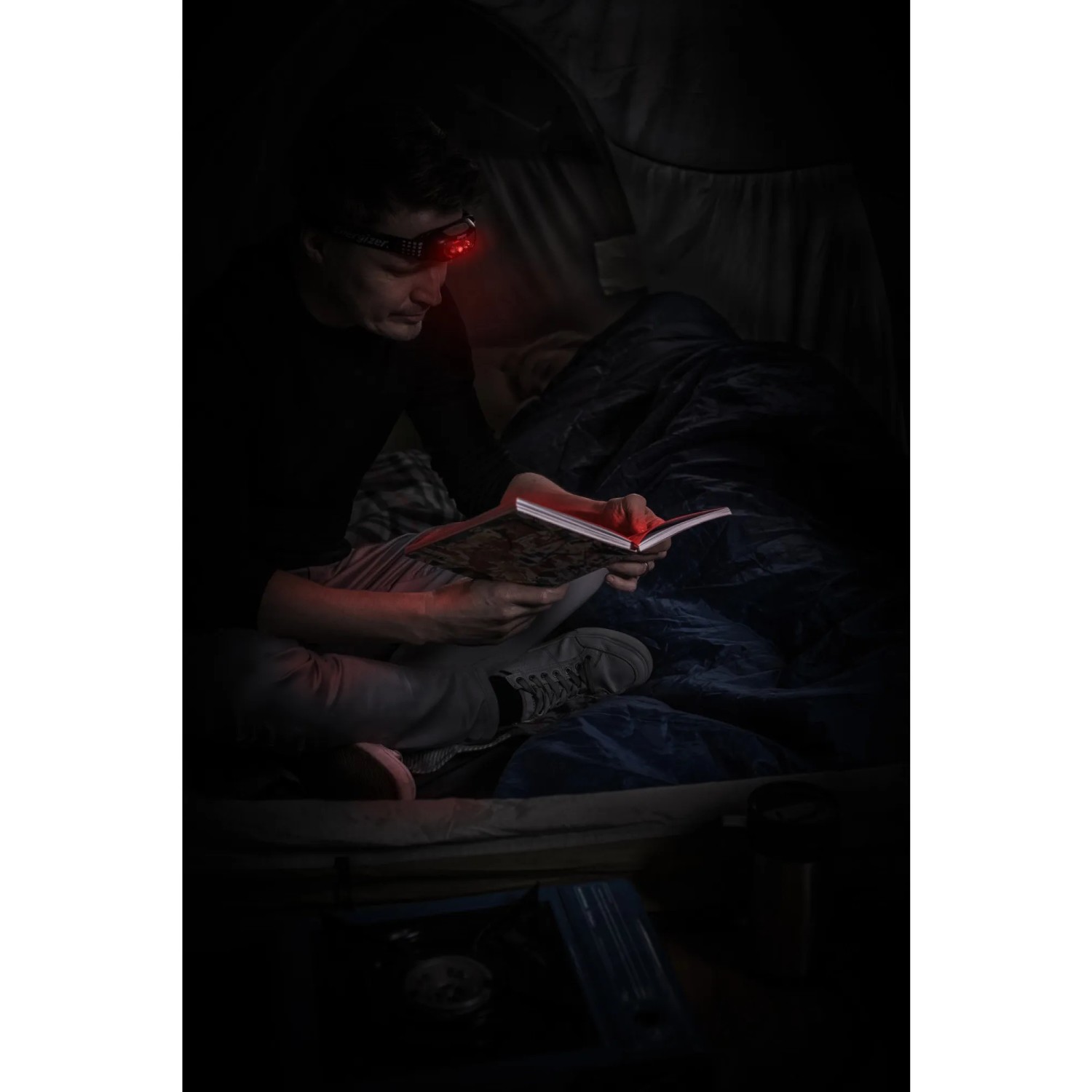 Mann liest im Zelt mit roter Energizer Kopflampe Universal + Headlamp.