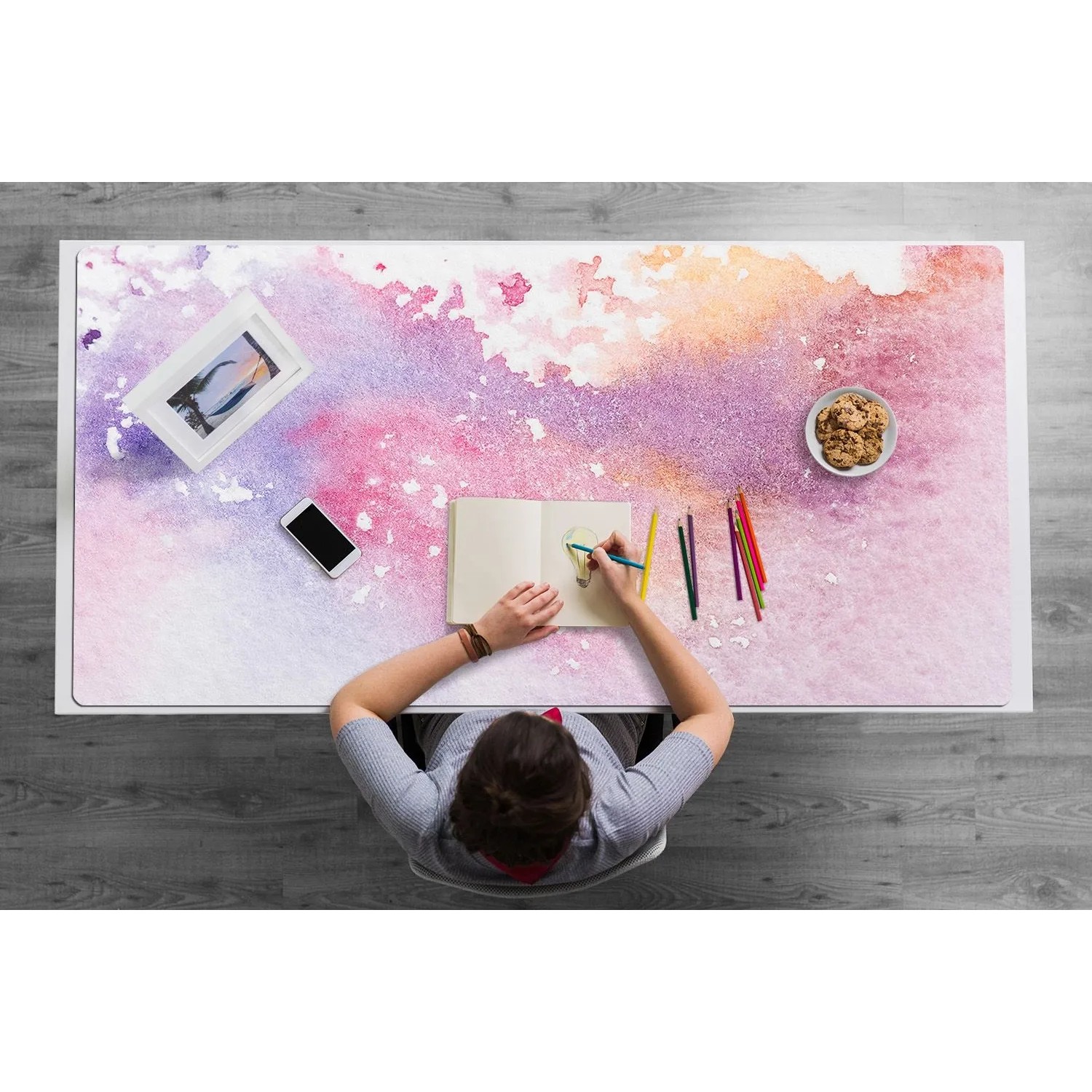 Bunte Schreibtischunterlage mit Süßigkeitenflecken-Design in Rosa, Lila, Orange. Person zeichnet am Schreibtisch. Bürobedarf.