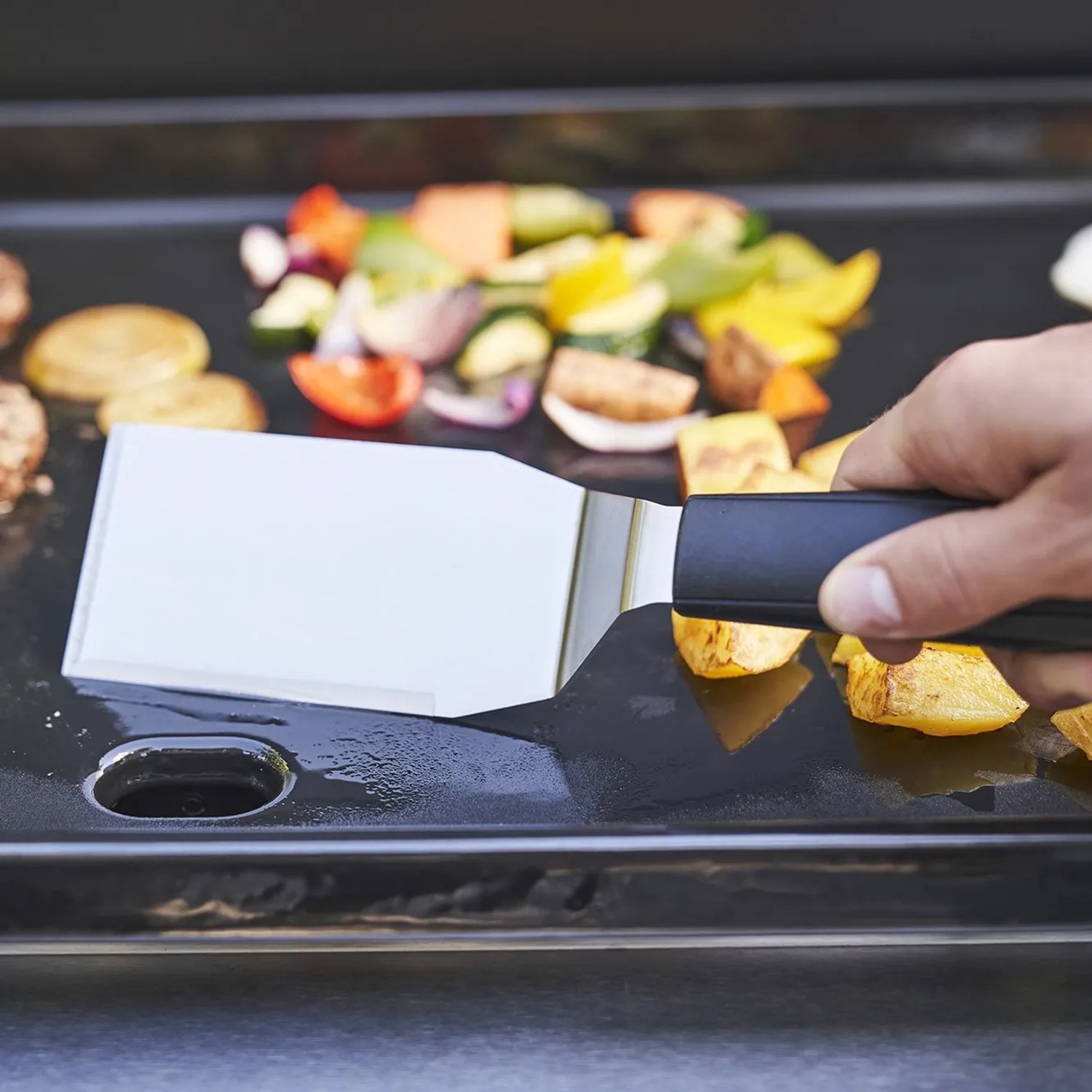 Char-Broil Griddle 3400 Gasgrill: Grillplatte mit Gemüse und Spatel in Aktion.