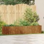 Langer, rechteckiger Pflanzkübel aus wetterfestem Stahl in Rostoptik, bepflanzt im Garten vor einem Holzzaun.