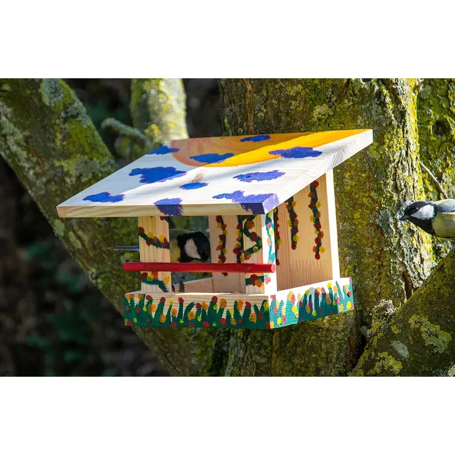 Bemaltes Dobar Vogelfutterhaus aus Kiefernholz am Baum mit Vogel, Bausatz 23x18x16 cm.