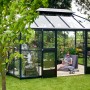 Juliana Gewächshaus Grand Oase 13 Anthrazit im Garten mit entspannender Person. Begehbares Gewächshaus mit viel Platz.