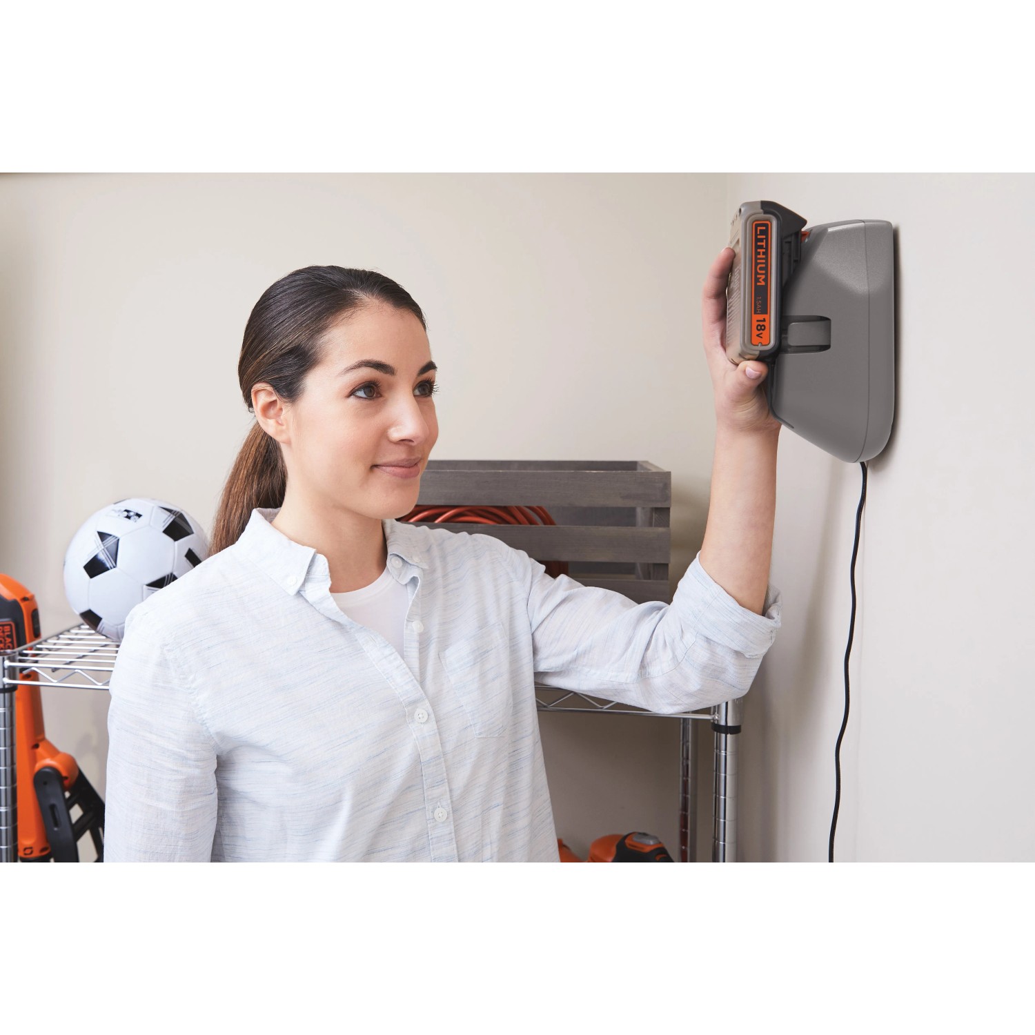 Frau lädt Black+Decker 18V Akku an Wandladestation. Akku und Ladegerät nicht enthalten.
