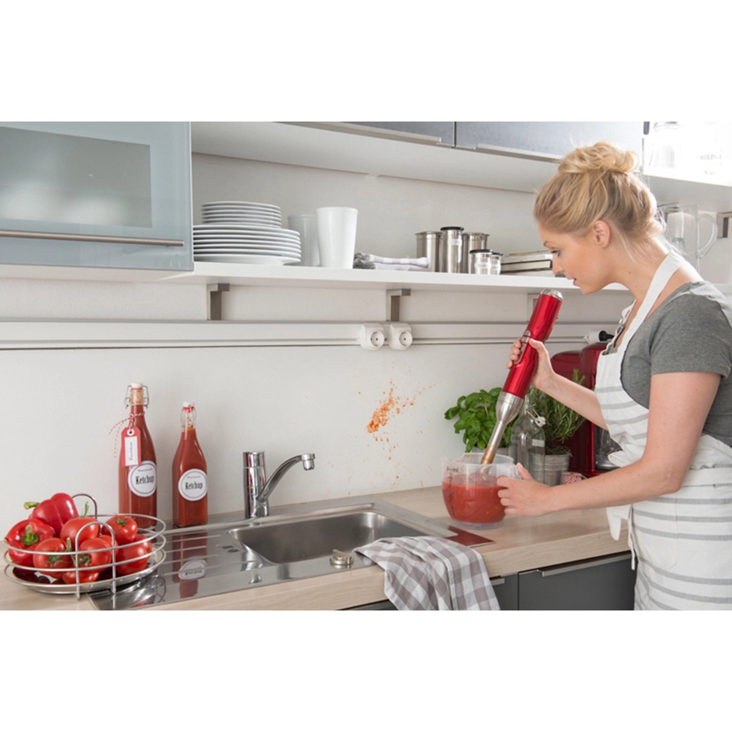 Frau mixt Tomatensoße mit einem roten Stabmixer in der Küche.