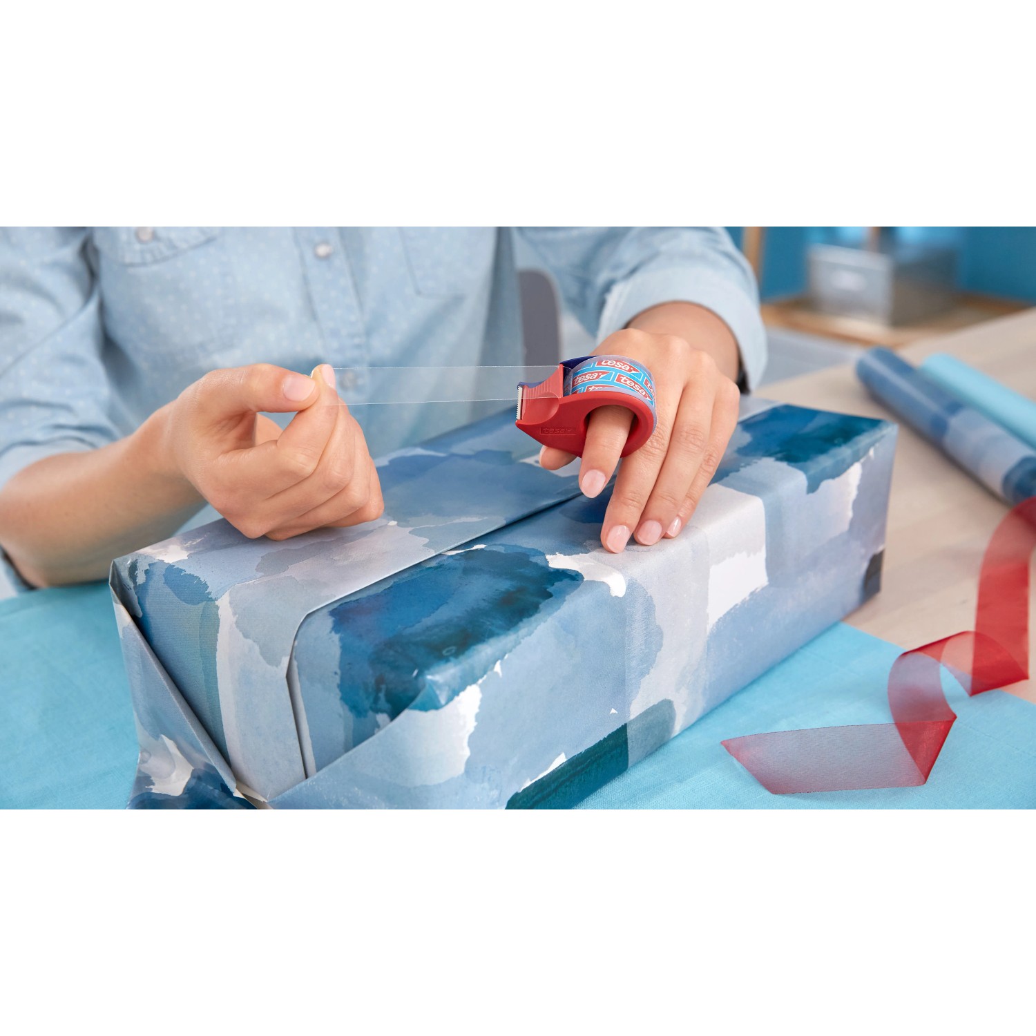 Frau verpackt Geschenk mit Tesa Film Kristall-Klar und Mini-Abroller am Finger.