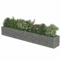 Langes Gabionen-Hochbeet aus verzinktem Stahl, mit grauen Steinen gefüllt und grünen Pflanzen sowie Blumen bepflanzt.