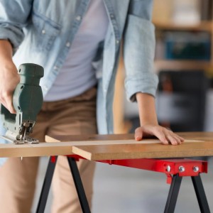 Person sägt Holz auf rotem Relaxdays Arbeitsbock (2er Set). Klappbarer Stahlbock mit Antirutsch-Auflage.
