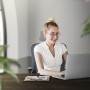 Frau sitzt auf grauem ML-Design Bürostuhl aus Mesh vor Laptop.