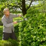 Mann schneidet Hecke mit Gardena EnergyCut 2in1 Hand-Heckenschere im Garten.