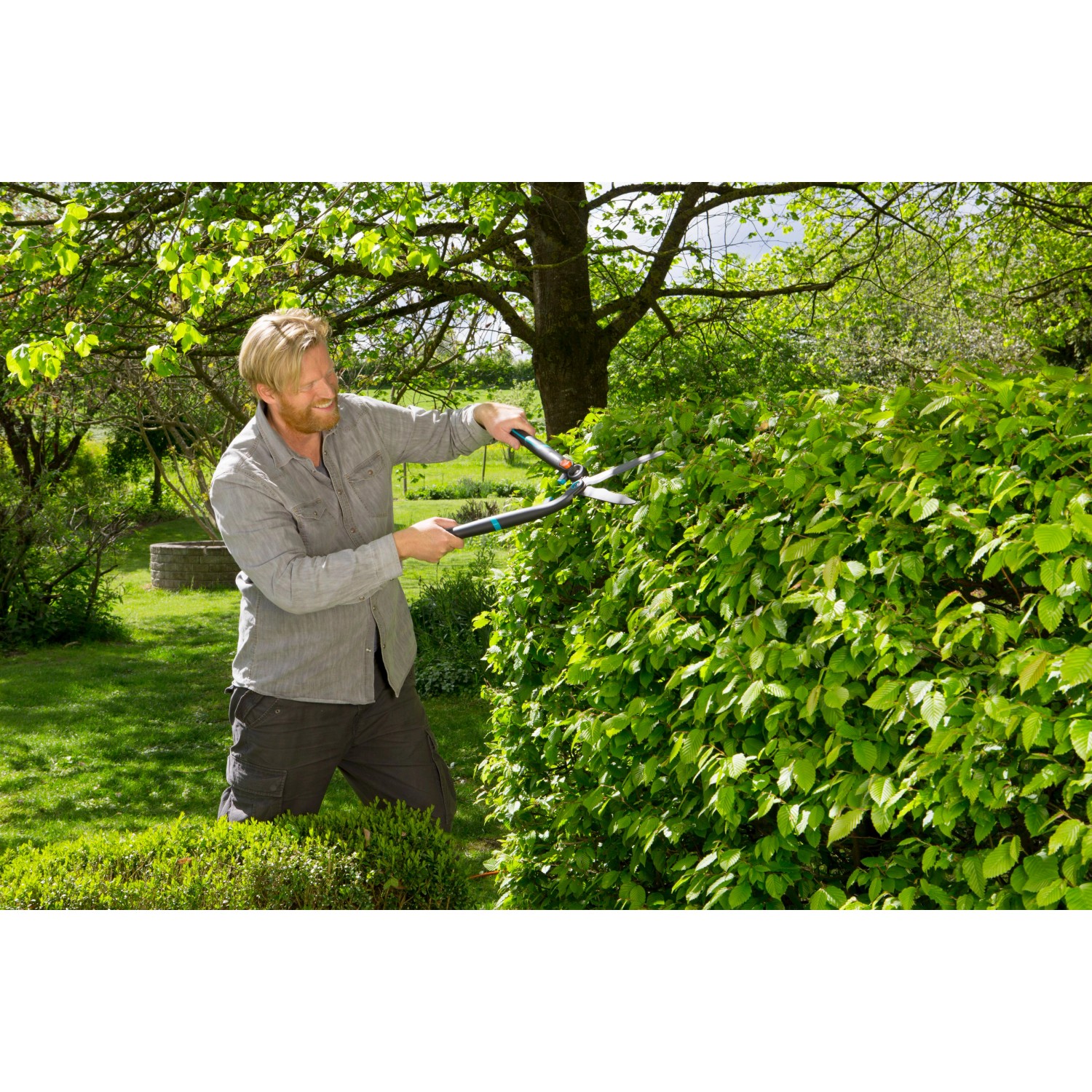 Mann schneidet Hecke mit Gardena EnergyCut 2in1 Hand-Heckenschere im Garten.