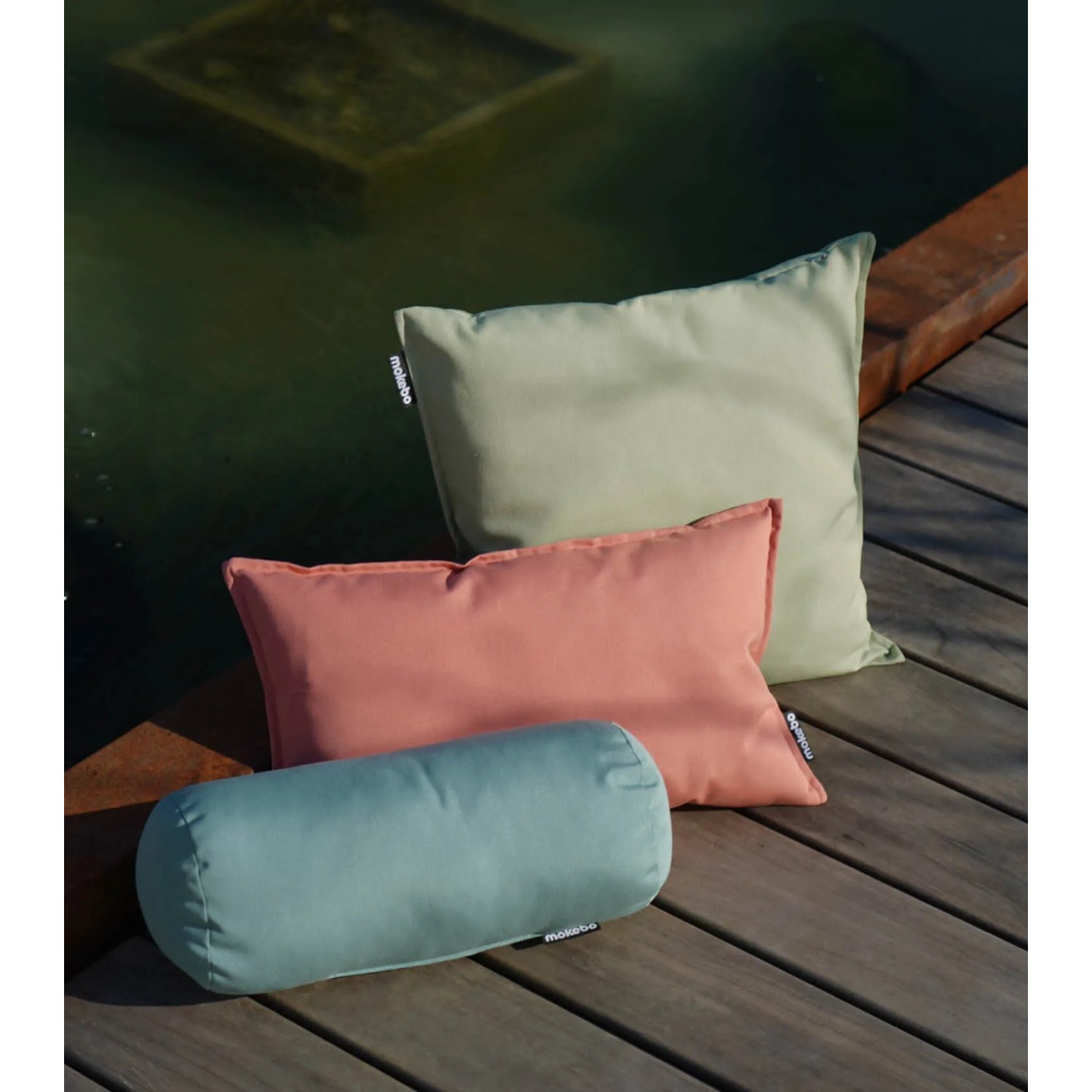 mokebo Outdoor Kissen Set: Lindgrünes Sofakissen, Nierenkissen und Rolle auf Holzterrasse.