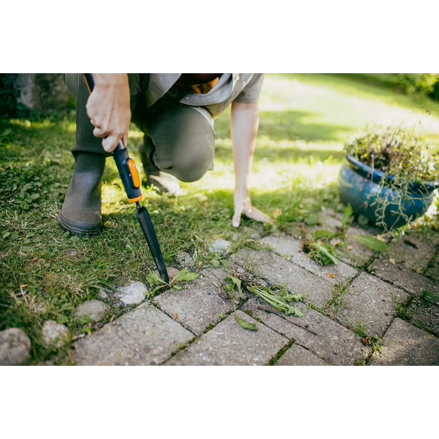 Anwendung des Fiskars Unkrautstechers OneClick im Garten auf Pflastersteinen.