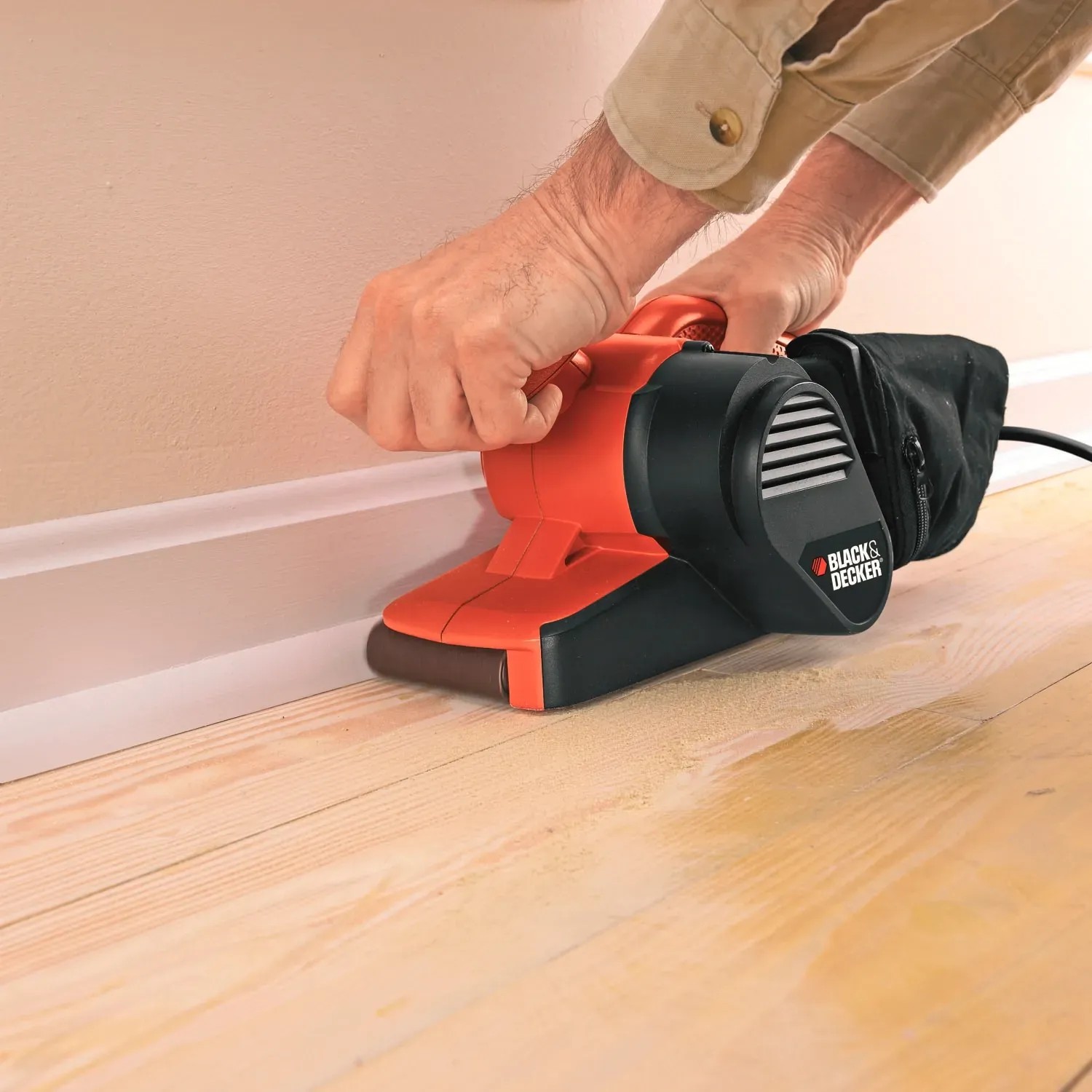 Black+Decker Bandschleifer KA86 beim Schleifen einer Sockelleiste. Die Schleifmaschine ist orange-schwarz.