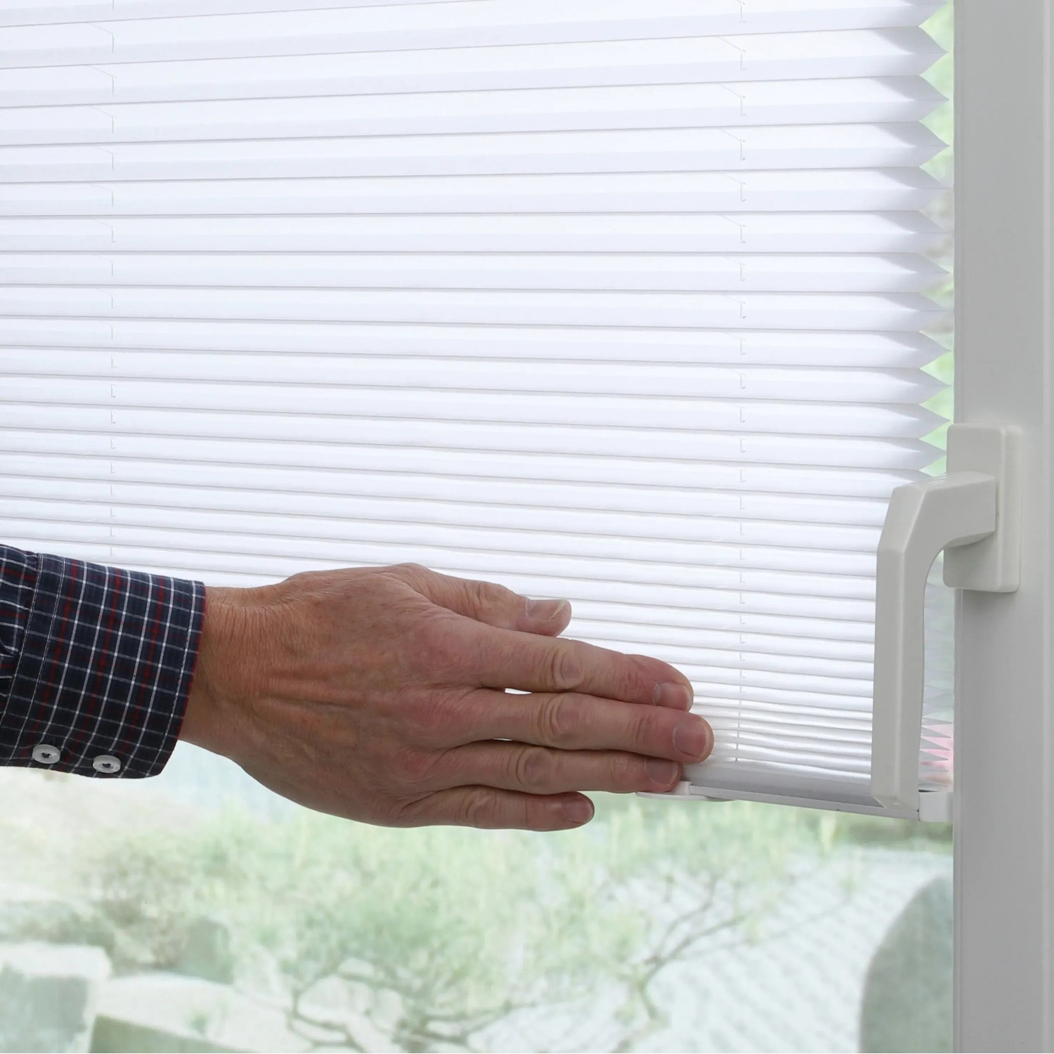 Weißes Gardinia Plissee Solo am Fenster mit Hand zur Bedienung. Lichtdurchlässiger Sichtschutz.