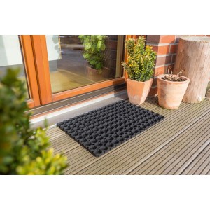 Schwarze ASTRA Gummi Fußmatte Quadro light, 40x60 cm, vor einer Haustür auf Holzterrasse.
