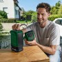 Mann hält Bosch UniversalSpeaker 18V-1 Akku-Bluetooth-Box und zweiten Lautsprecher auf Werkbank. Kompaktes Akkugerät für kabelloses Streaming.