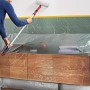Frau streicht Wand mit Farbroller, Möbel mit Tesa Abdeckfolie geschützt.