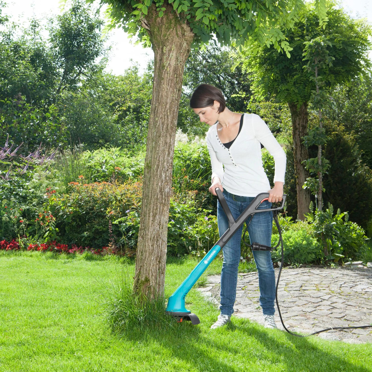 Frau trimmt Rasenkante mit Gardena Elektro-Rasentrimmer SmallCut 300/23 im Garten.