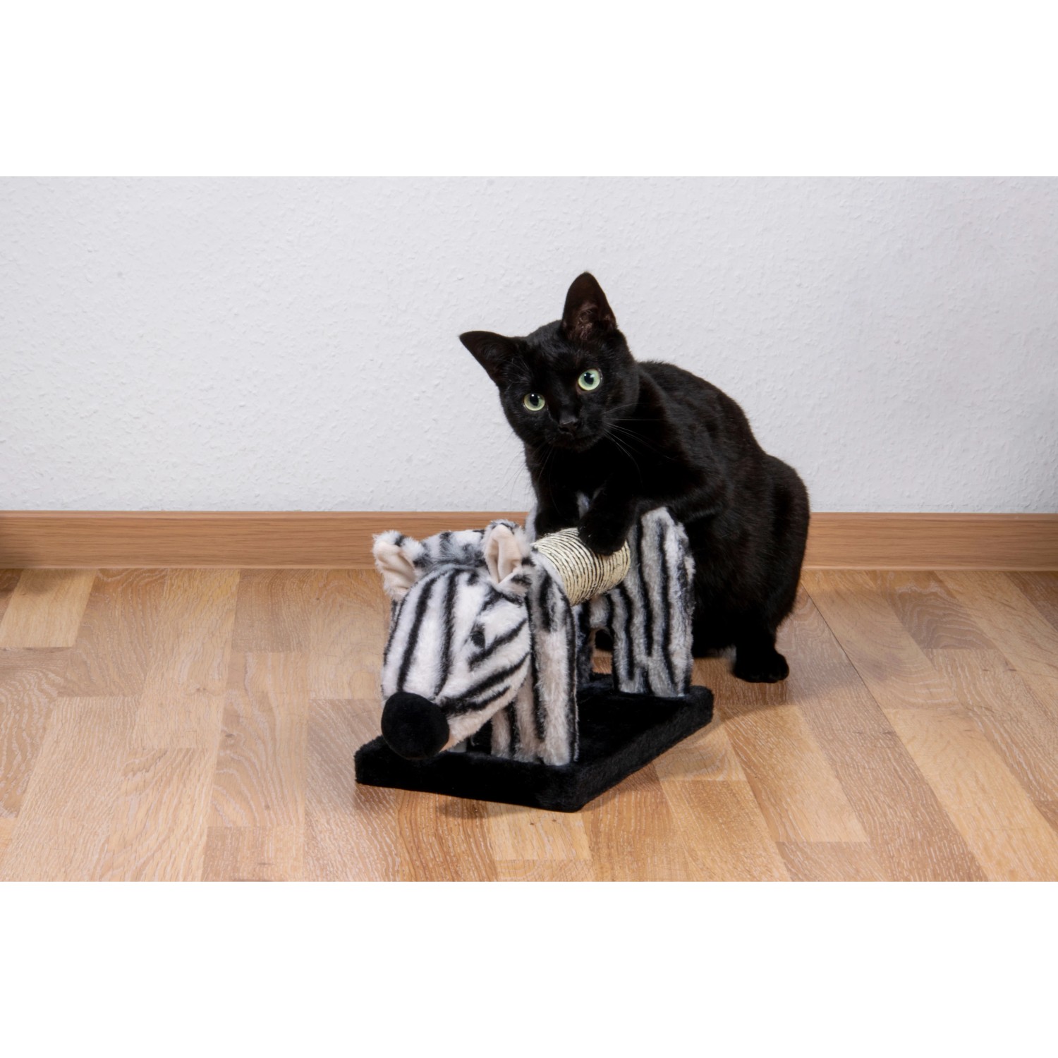 Schwarze Katze spielt mit Dobar Kratztier-Set (Zebra). Katzenbürste aus Sisal und Plüsch, 51x16,5x18 cm.