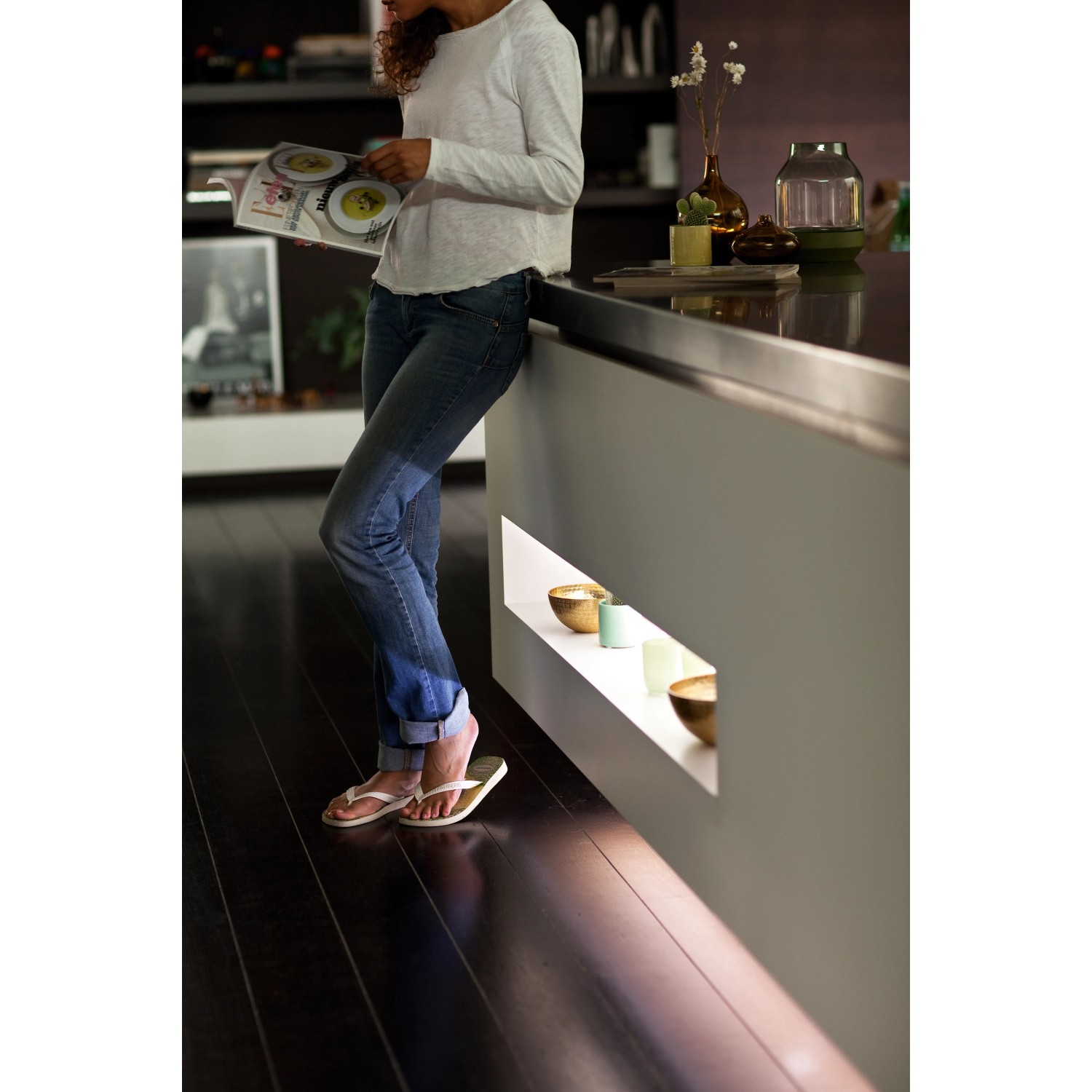 Frau liest neben Philips Hue Lightstrip Plus unter Kücheninsel. Ambientebeleuchtung.