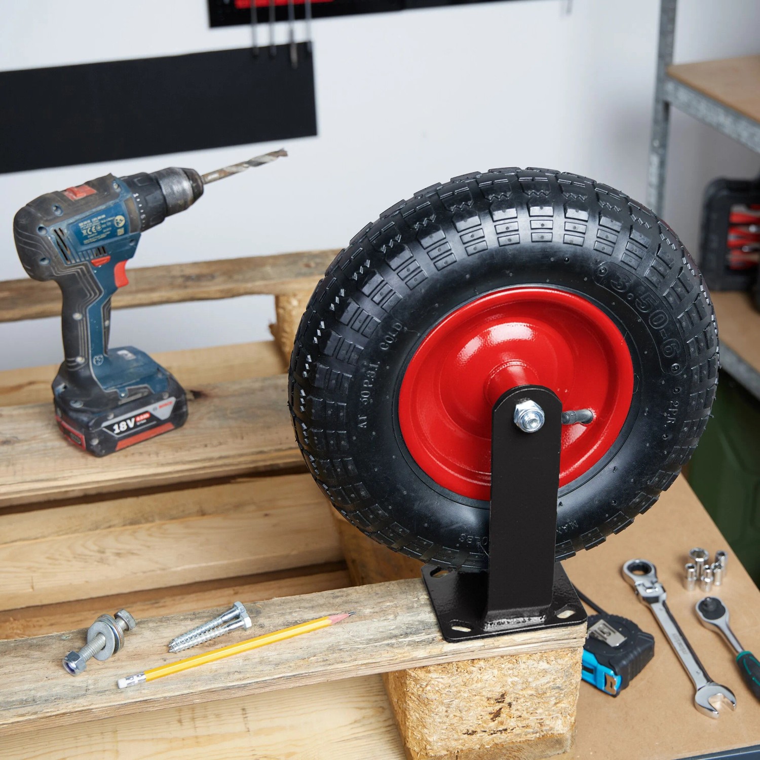 Schwarze, luftbereifte Bockrolle mit roter Felge und Stahl-Montageplatte auf Holzpalette. Ideal für Schwerlast-Transport.
