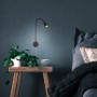 Schwenkbare, schwarze Briloner LED Bettleuchte Tusa, montiert an blauer Wand über Nachttisch mit Pflanze.