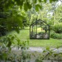 Schwarzes Halls Gewächshaus Popular 106 mit 6,2 m² im Garten, umgeben von Bäumen.
