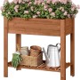 Braunes Holz-Hochbeet mit Blumenkasten, bepflanzt mit rosa Blumen. Unten Ablage für Gartengeräte. Ideal für Balkon & Garten.