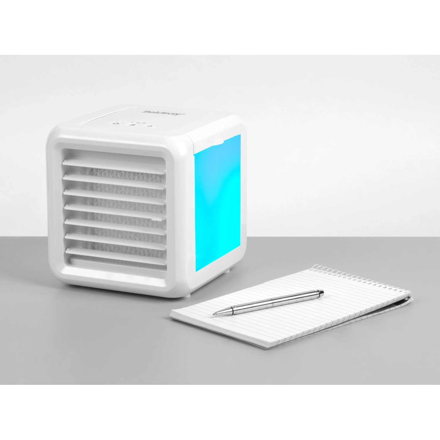 Weißer Mini Luftkühler mit blauer LED, Notizblock und Stift auf einem Tisch.