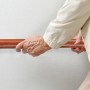 Ältere Hand greift braunen Handlauf aus Aluminium mit Eiche-Optik an weißer Wand für sicheren Halt.
