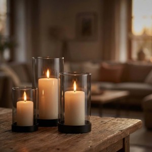 Drei unterschiedlich große Rauchglas-Windlichter mit schwarzen Eisenfüßen und brennenden Kerzen auf einem Holztisch. Kerzenhalter Set für stimmungsvolle Dekoration.
