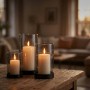 Drei unterschiedlich große Rauchglas-Windlichter mit schwarzen Eisenfüßen und brennenden Kerzen auf einem Holztisch. Kerzenhalter Set für stimmungsvolle Dekoration.