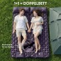 Paar auf zwei lila Evocamp Ultraleicht Isomatten mit Kissen, per Druckknöpfe verbunden als Doppelbett auf Gras vor Zelt.