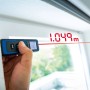 LUX-TOOLS Laserentfernungsmesser im Einsatz, Messwerkzeug mit rotem Laserstrahl am Fenster.