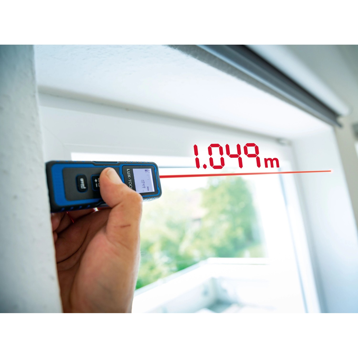 LUX-TOOLS Laserentfernungsmesser im Einsatz, Messwerkzeug mit rotem Laserstrahl am Fenster.