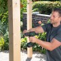 Mann schraubt mit Bosch Akku-Bohrschrauber AdvancedDrill 18V-80 ein Brett im Garten.