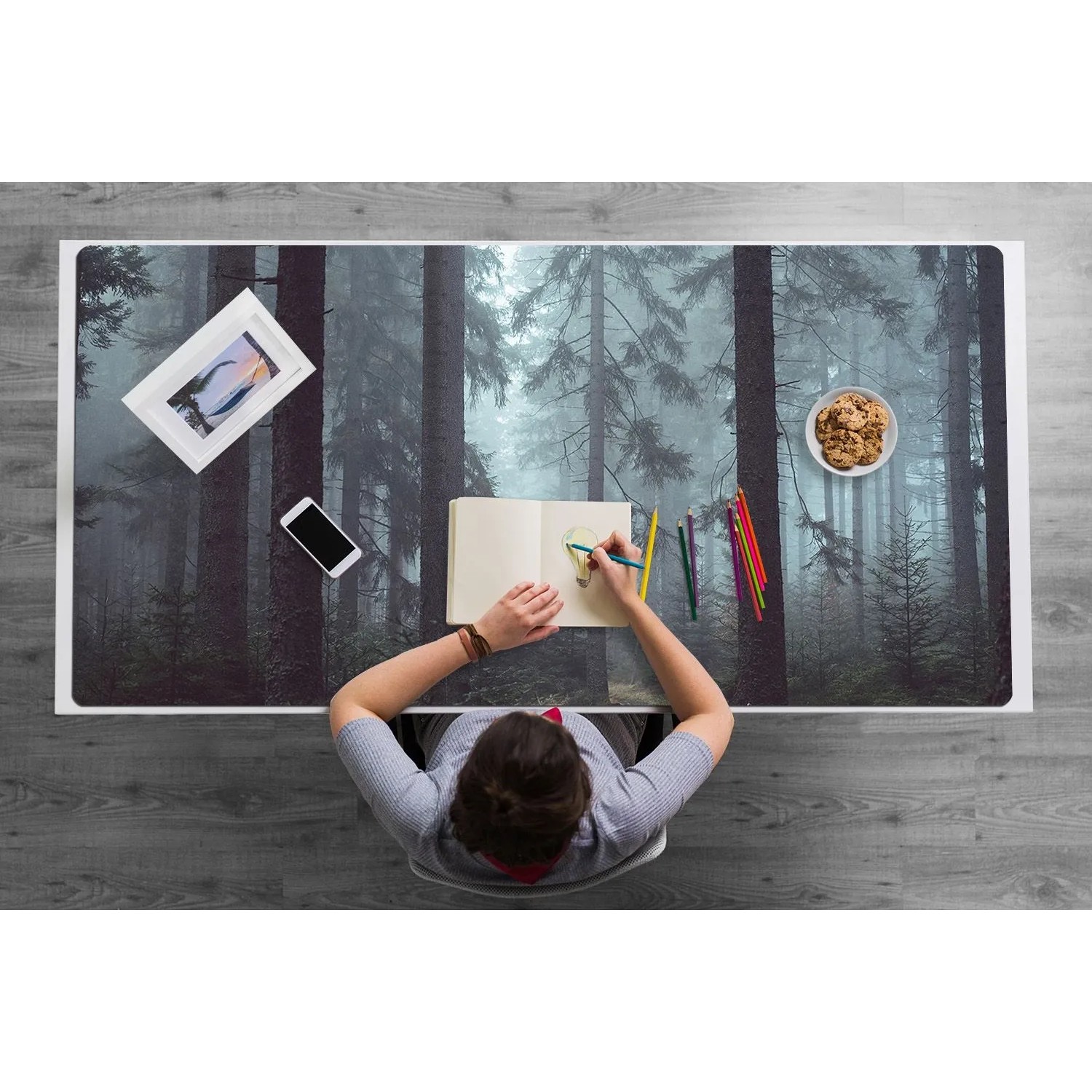 Graue Schreibtischunterlage mit Nebelwald-Motiv auf Schreibtisch, Person zeichnet. Schützt Arbeitsplatz, ideal für Bürobedarf.