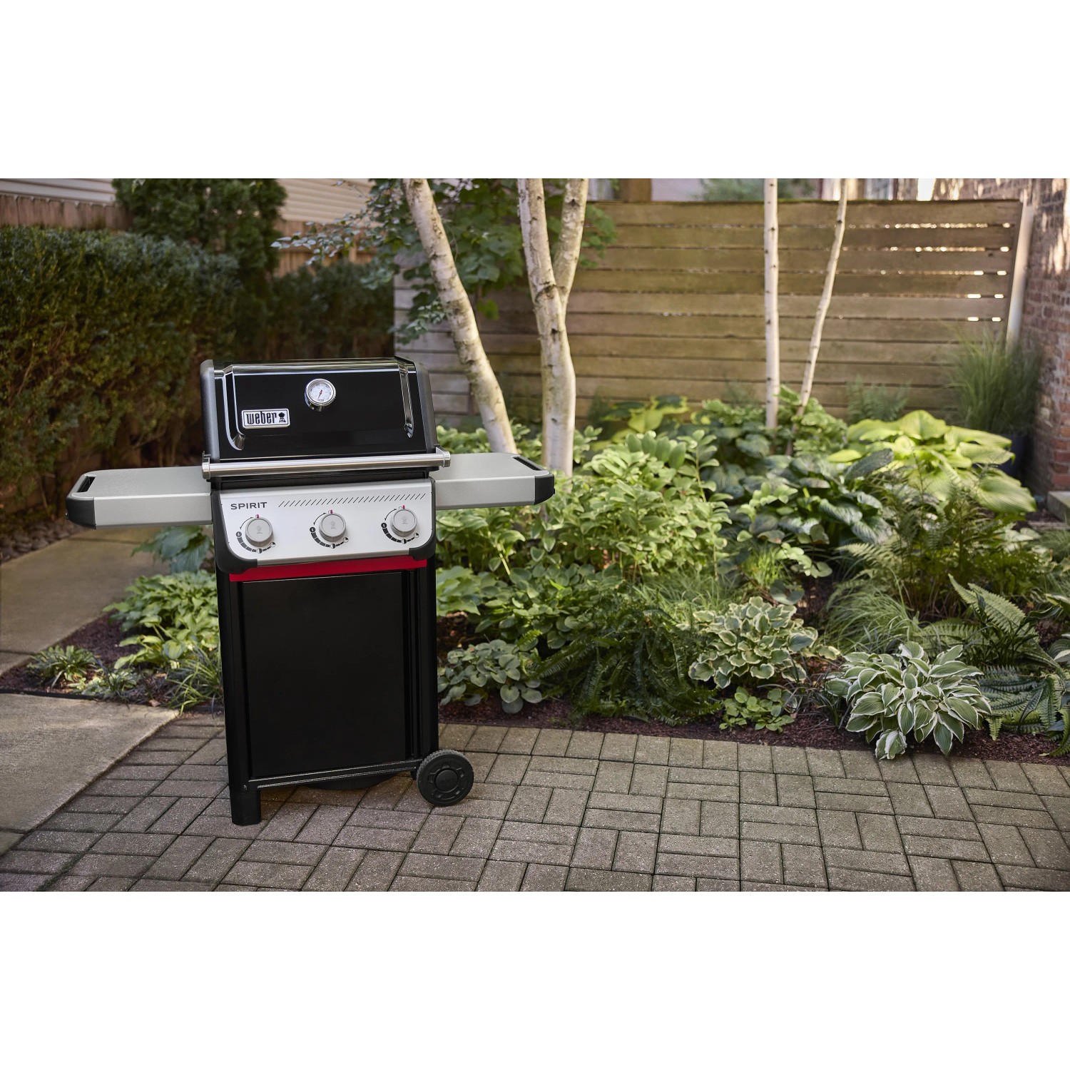 Schwarzer Weber Gasgrill E-310 Spirit 2025 mit 3 Brennern vor Gartenkulisse.