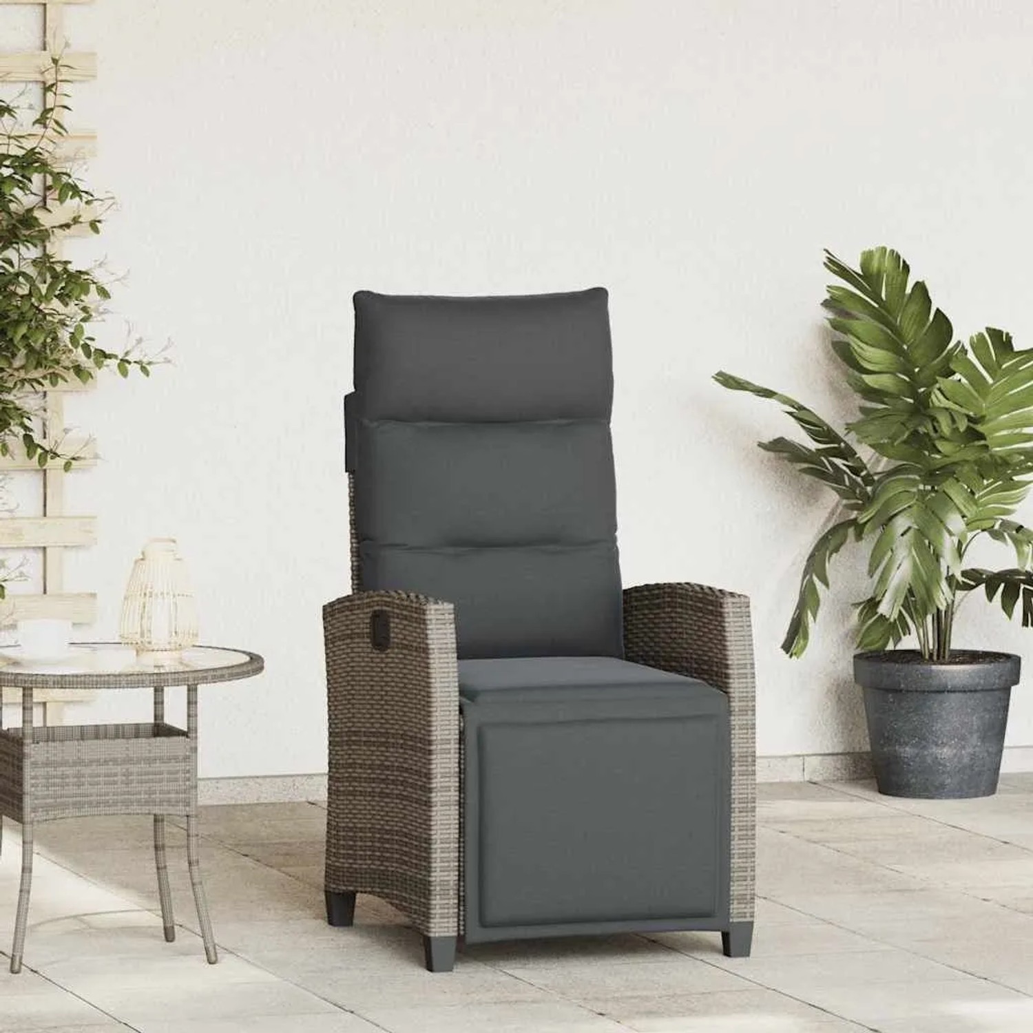 Grauer Poly Rattan Gartensessel mit dunklen Kissen, ausziehbarer Fußstütze und Beistelltisch auf Terrasse.