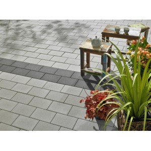 Verlegte, silbergraue Beton Pflastersteine Vero (22,5x15x6cm) mit feiner Oberfläche auf Terrasse mit Tisch und Pflanzen.